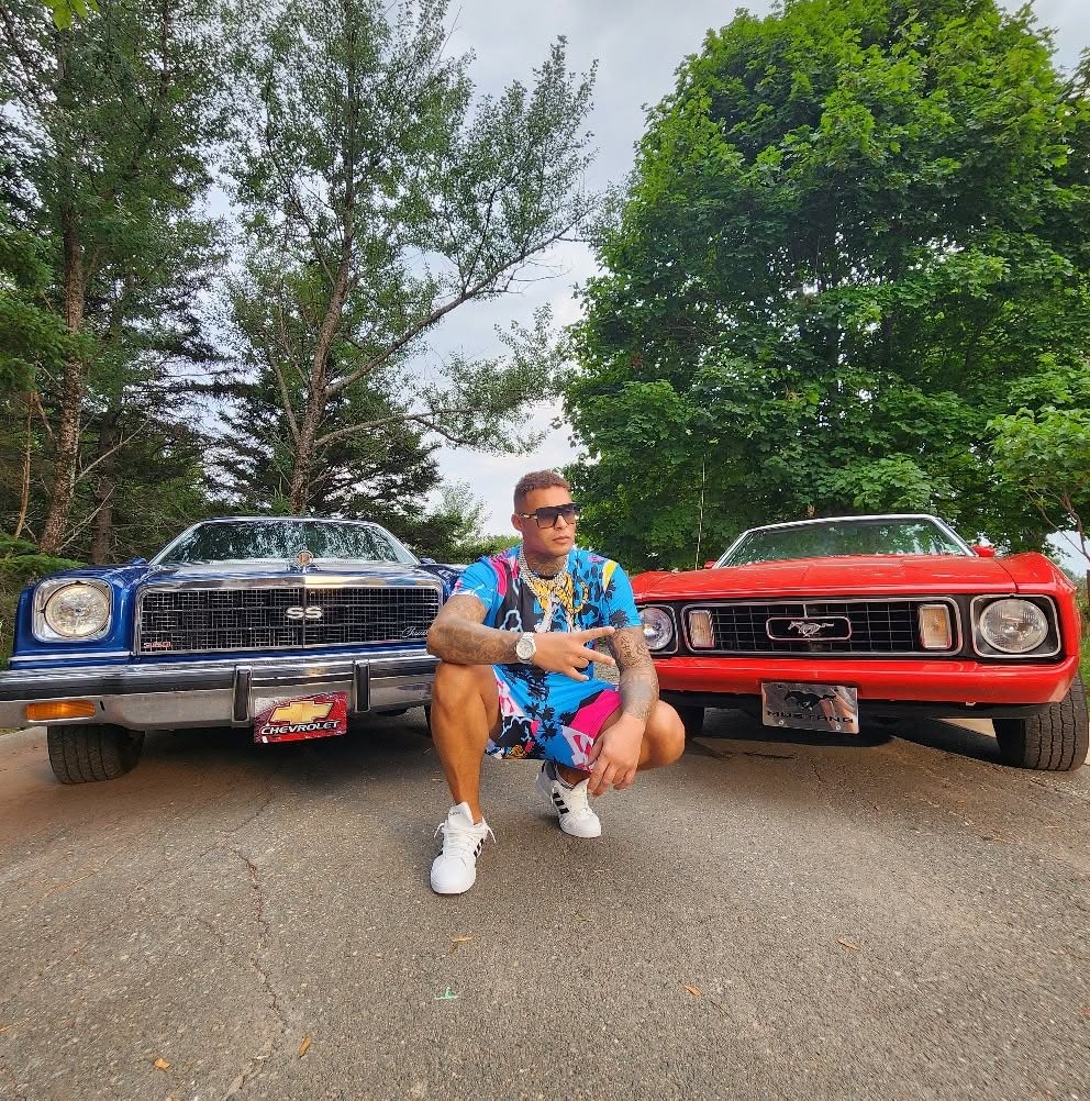Andru Winter crouching between a blue and a red classic car